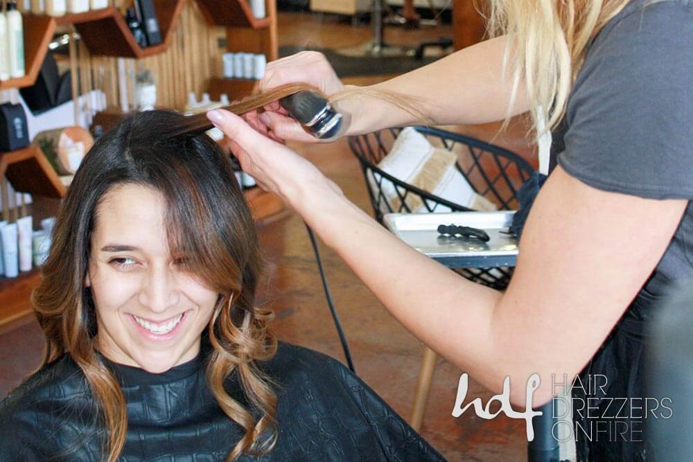 A client smiles while having her hair flat-ironed