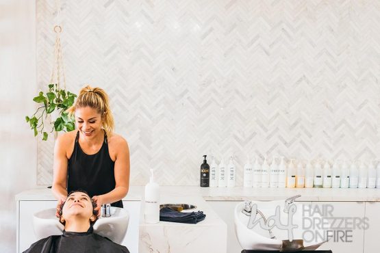 Hair stylist smiles as she massages client's head at a rinse station