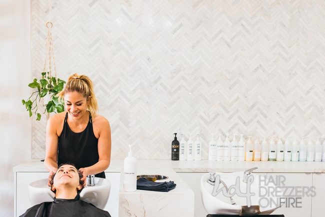 Hair stylist smiles as she massages client's head at a rinse station