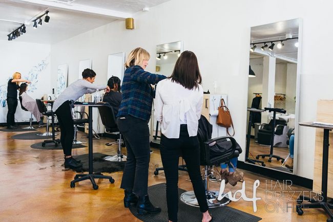 Two hair stylists work with their backs to the camera