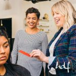 Two hair stylists smile, holding a red object