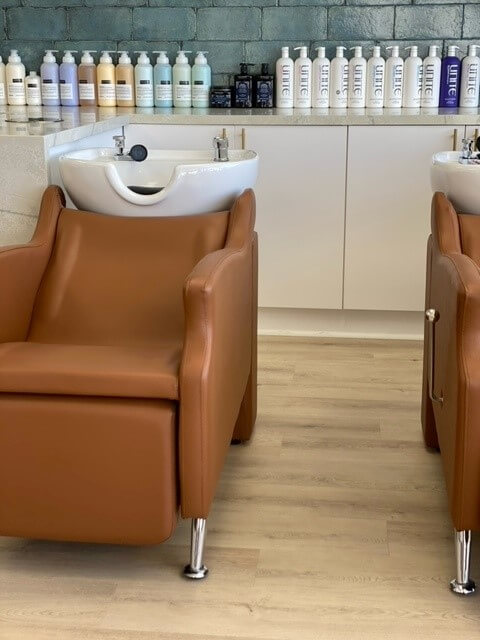 Hair rinsing station and hair products lined up on a shelf behind